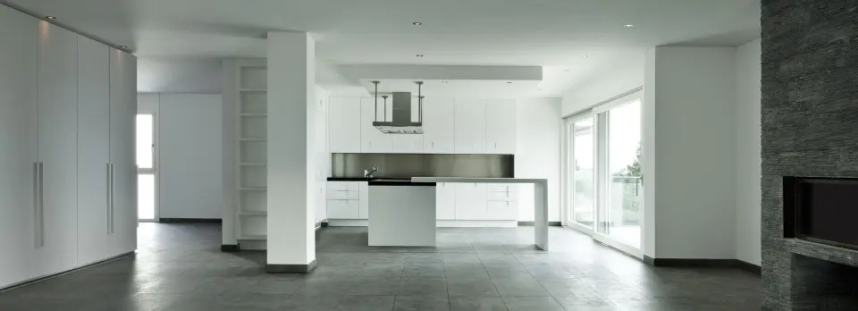 Modern open-plan interior with a white kitchen, tiled floor, built-in cabinetry, fireplace and large glass doors.